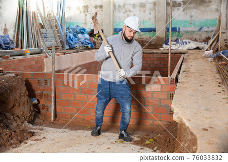 Guy excavating ground with mattock at building site Guy excavating ground with mattock at building site 76033832