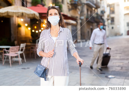 Young woman in medical mask walking around city with suitcase Young woman in medical mask walking around city with suitcase 76033890