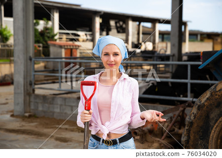 Female owner of dairy farm standing near tractor Female owner of dairy farm standing near tractor 76034020