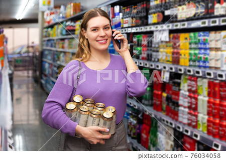 woman buys canned beer in hypermarket and talking on mobile phone 76034058