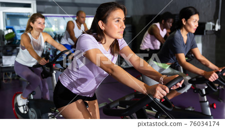 Woman training on stationary bike in gym Woman training on stationary bike in gym 76034174