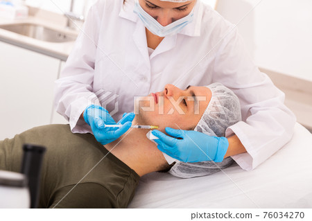 Man getting face injections at aesthetic clinic Man getting face injections at aesthetic clinic 76034270