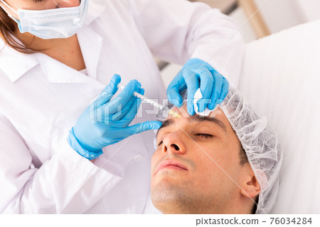 Man getting face injections at aesthetic clinic 76034284