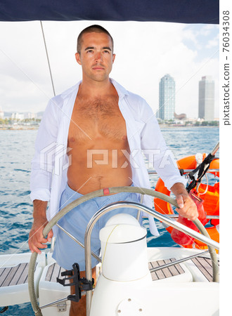 Man steering yacht along Barcelona coastline 76034308