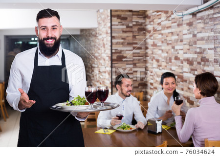 young waiter serving dear restaurant guests young waiter serving dear restaurant guests 76034624