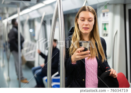 Young woman browsing on phone in metro car 76034719