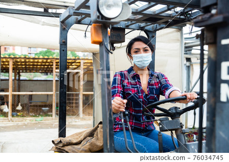 Masked hispanic woman sits behind the wheel of a tractor autocar during a pandemic. 76034745