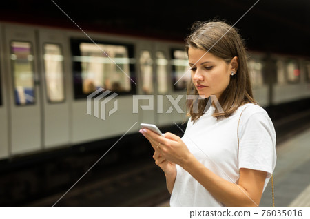 Woman waiting subway car using phone 76035016