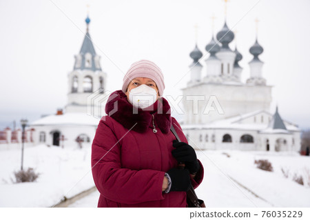 Portrait of a woman in a protective mask in winter against the background of the Resurrection monastery in Murom. Portrait of a woman in a protective mask in winter against the background of the Resurrection monastery in Murom. 76035229