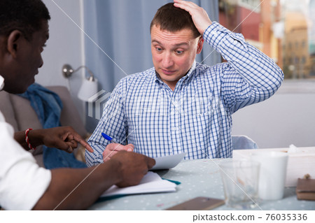 Upset two men in home interior, filling up documents Upset two men in home interior, filling up documents 76035336