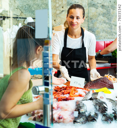female fishmonger showing variety of fresh fish and seafoods female fishmonger showing variety of fresh fish and seafoods 76035342