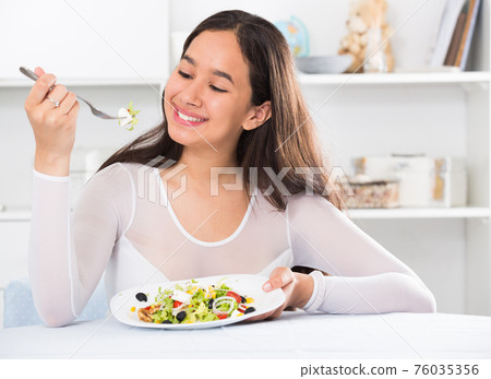 Positive young female eating salad Positive young female eating salad 76035356