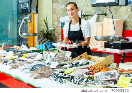 Female fishmonger offering fresh sea bass Female fishmonger offering fresh sea bass 76035363