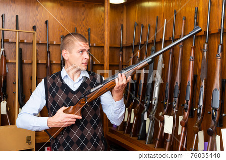 Man examining hunting shotgun before buying in gun store Man examining hunting shotgun before buying in gun store 76035440