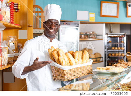 Jolly African American baker holding baguettes 76035605