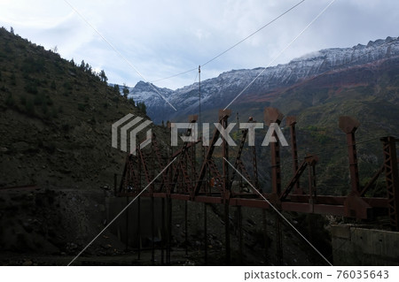 Construction of a new bridge in the Himalayan Mountains in the early cloudy morning. Two people at a height are building a bridge. Construction of a new bridge in the Himalayan Mountains in the early cloudy morning. Two people at a height are building a bridge. 76035643