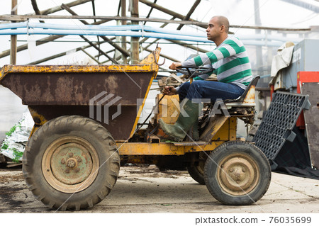 Latin american male farmer driving a mini dump truck, drives out to throw out the weeds. Latin american male farmer driving a mini dump truck, drives out to throw out the weeds. 76035699