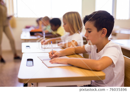 Boy sits at desk next to diligent elementary school students Boy sits at desk next to diligent elementary school students 76035896