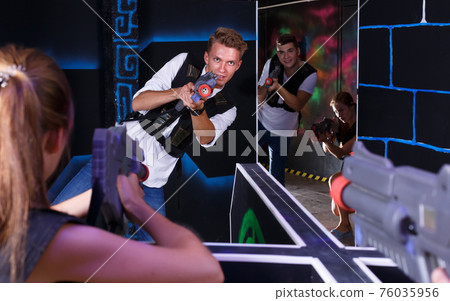 Positive girls and guys playing laser tag game opposite each other Positive girls and guys playing laser tag game opposite each other 76035956