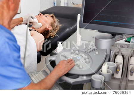 Elderly man sonographer using ultrasonography machine checking female patient in hospital diagnostic room 76036354