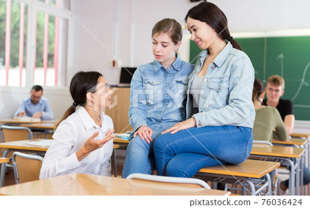 Young girls are sitting at the desk and talking about boys in the classroom Young girls are sitting at the desk and talking about boys in the classroom 76036424