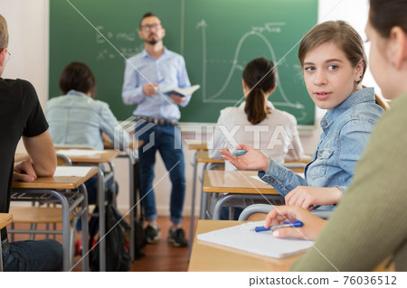Young girls are sitting at the desk and talking in time lecture in the classroom 76036512