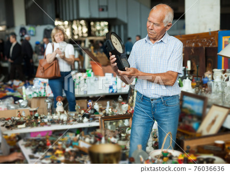 Gray-haired mature man chooses rare clock at flea market 76036636