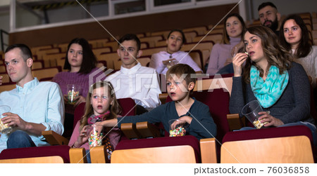 Enthusiastic audience eating popcorn and watching a movie Enthusiastic audience eating popcorn and watching a movie 76036858