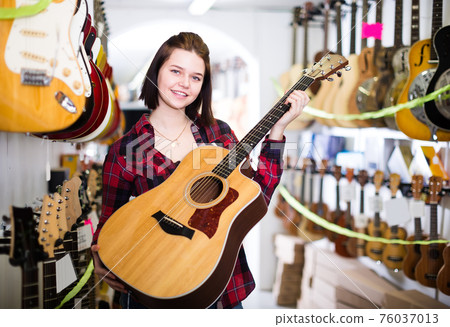 Nice teen girl examining various acoustic guitars 76037013