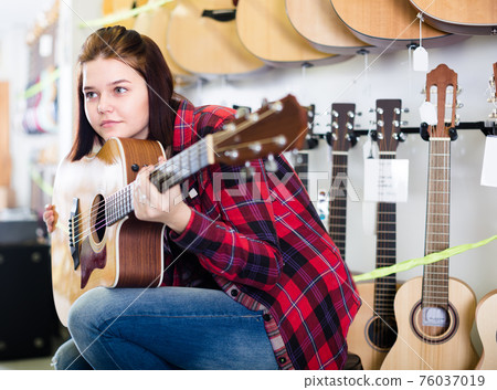 Smiling teen girl examining various acoustic guitars 76037019