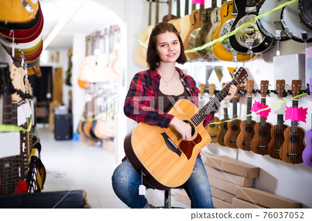 Customer girl is deciding on acoustic guitar 76037052