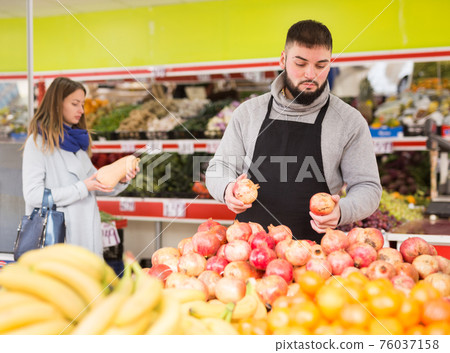 Positive man in apron selling ripe pomegranates 76037158