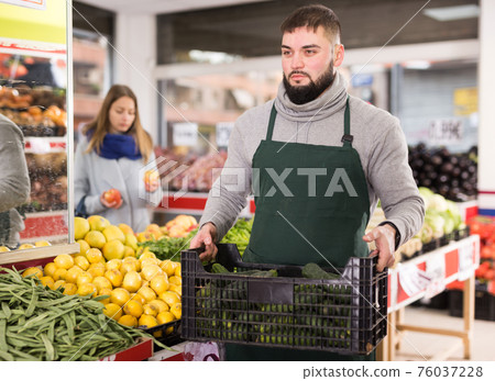 Positive seller in apron working in vegetables market 76037228
