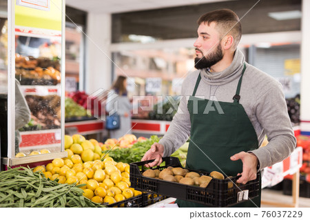 Man seller moving box of kiwi in grocery shop 76037229