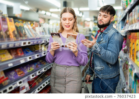 Happy young couple looking for sweet chocolate in grocery store 76037423