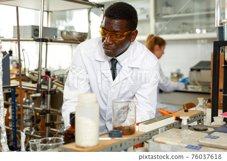 Man lab technician in glasses performing experiments and writing results Man lab technician in glasses performing experiments and writing results 76037618
