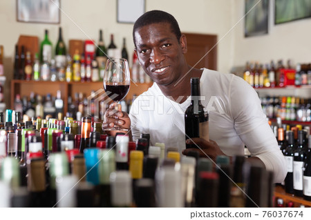 Confident african american male winemaker inspecting quality of red wine, checking it in wine store 76037674