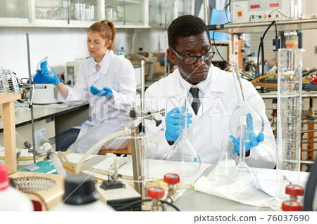 Man proffesional lab scientist in glasses working with reagents and test tubes Man proffesional lab scientist in glasses working with reagents and test tubes 76037690