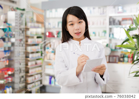 Chinese female looking medicine with notebook near shelves in pharmacy 76038042