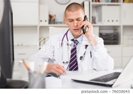 doctor talking on phone and making notes 76038043