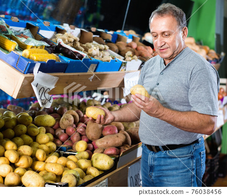 Smiling male is choosing potato in the supermarket. Smiling male is choosing potato in the supermarket. 76038456