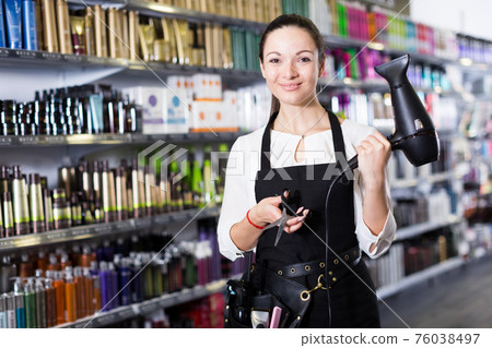 Female hairdresser in apron holding blow dryer and hair cutters 76038497