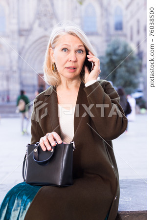 Mature positive female talking on phone in the historical city center Mature positive female talking on phone in the historical city center 76038500