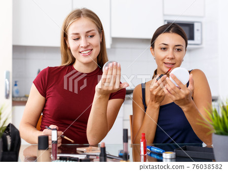 Female friends applying cosmetics Female friends applying cosmetics 76038582