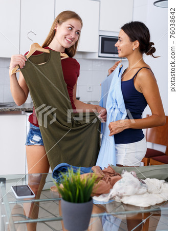 Smiling young women friends chatting and looking at clothes together Smiling young women friends chatting and looking at clothes together 76038642