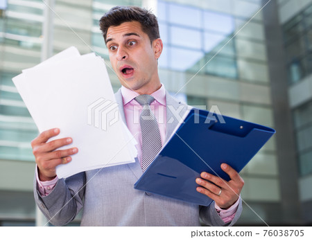 Shocked businessman reading papers Shocked businessman reading papers 76038705