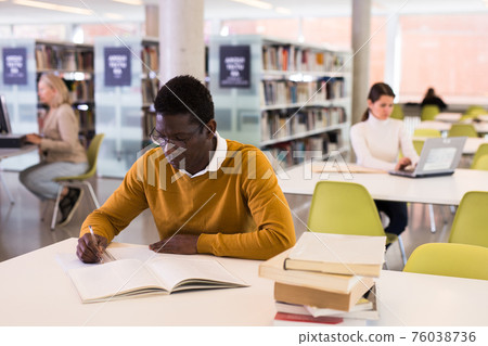 Intelligent african-american male student engaged in research working with books in university library 76038736