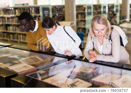 Teacher and adult students view rare books in a library showcase 76038737