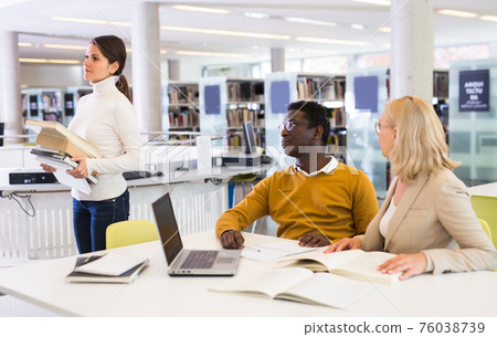 Teacher and adult students talking in the library 76038739