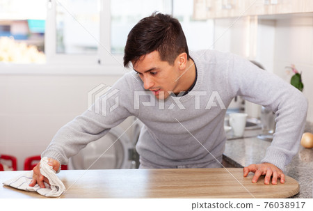 Man wipes a kitchen table with a rag Man wipes a kitchen table with a rag 76038917